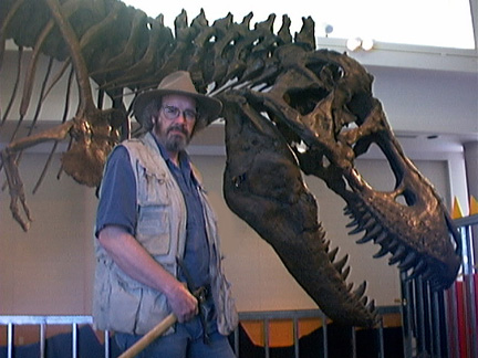 Jack Horner, holding rock hammer in front of a T-rex skeleton at the Museum of the Rockies